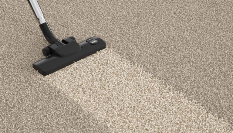 Aspirapolvere che pulisce una moquette beige a pelo corto, con evidente differenza tra la striscia pulita e quella da pulire