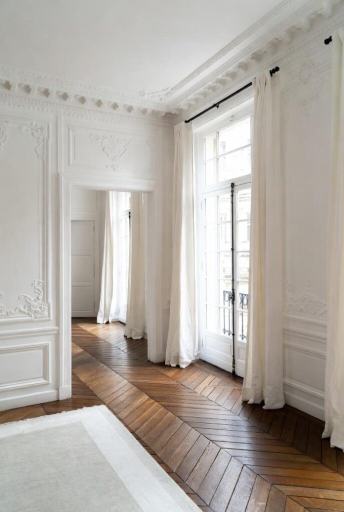 Arredare in stile parigino con corridoio elegante: pareti bianche modanature stucchi, parquet spina di pesce, tende lino e finestre luminose