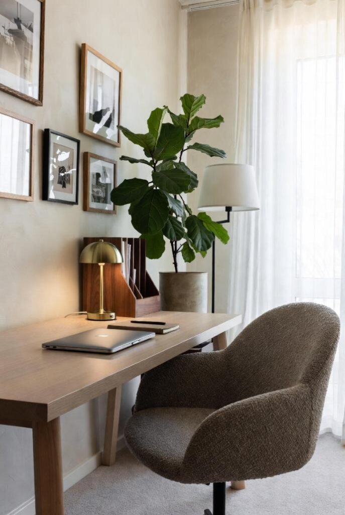 Arredare casa con colori neutri in home office, scrivania legno chiaro sedia bouclé greige, pianta felce lampada ottone.