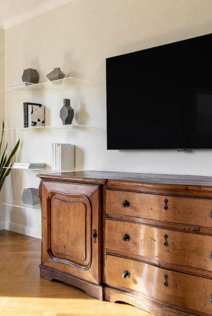 Credenza antica del '700 bilanciata con TV smart ultrasottile e mensole in vetro temperato: come abbinare arredamento antico e moderno senza caos.