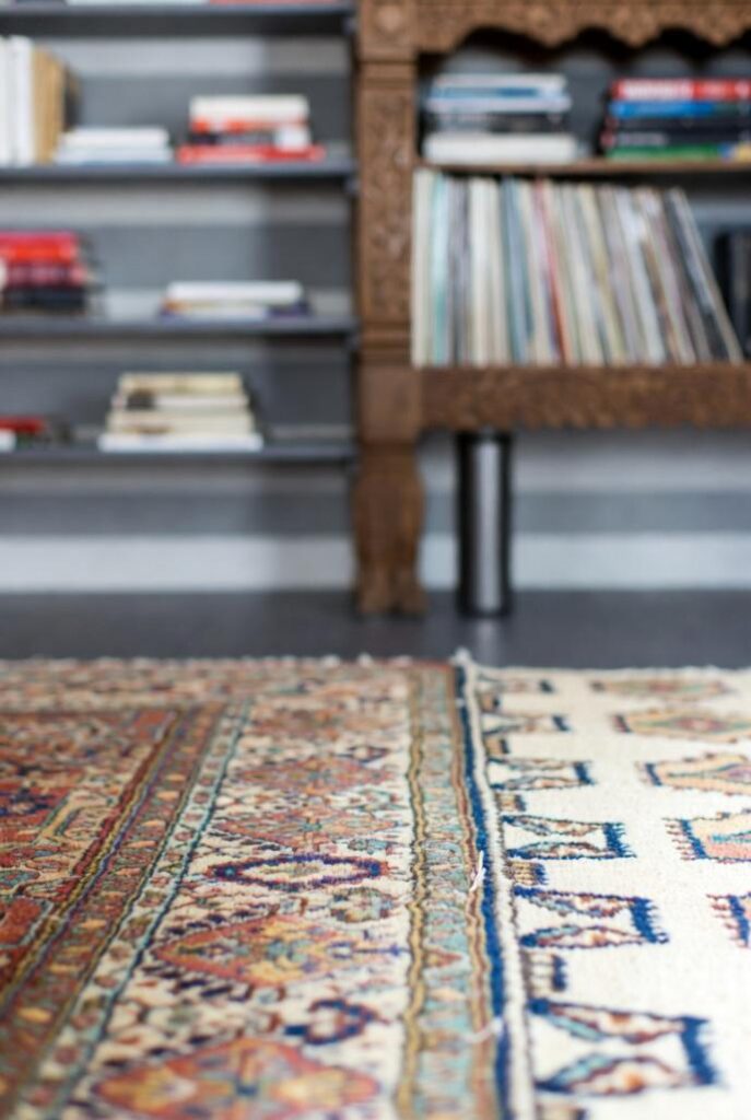 Pareti wallpaper moderno con mensole antiche, tappeti persiano-kilim e specchio convesso: dettagli per abbinare arredamento antico e moderno.