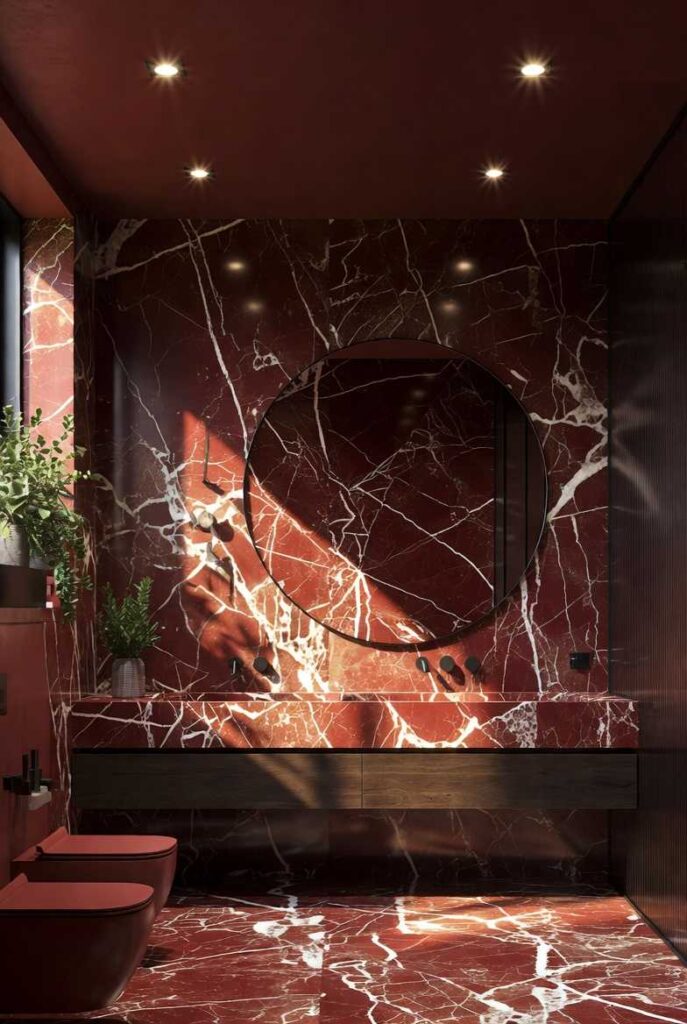 Interno di un bagno di lusso moderno con pareti e pavimenti in marmo rosso Verona a grandi venature bianche, lavabo integrato in pietra, specchio circolare e illuminazione calda soffusa.
