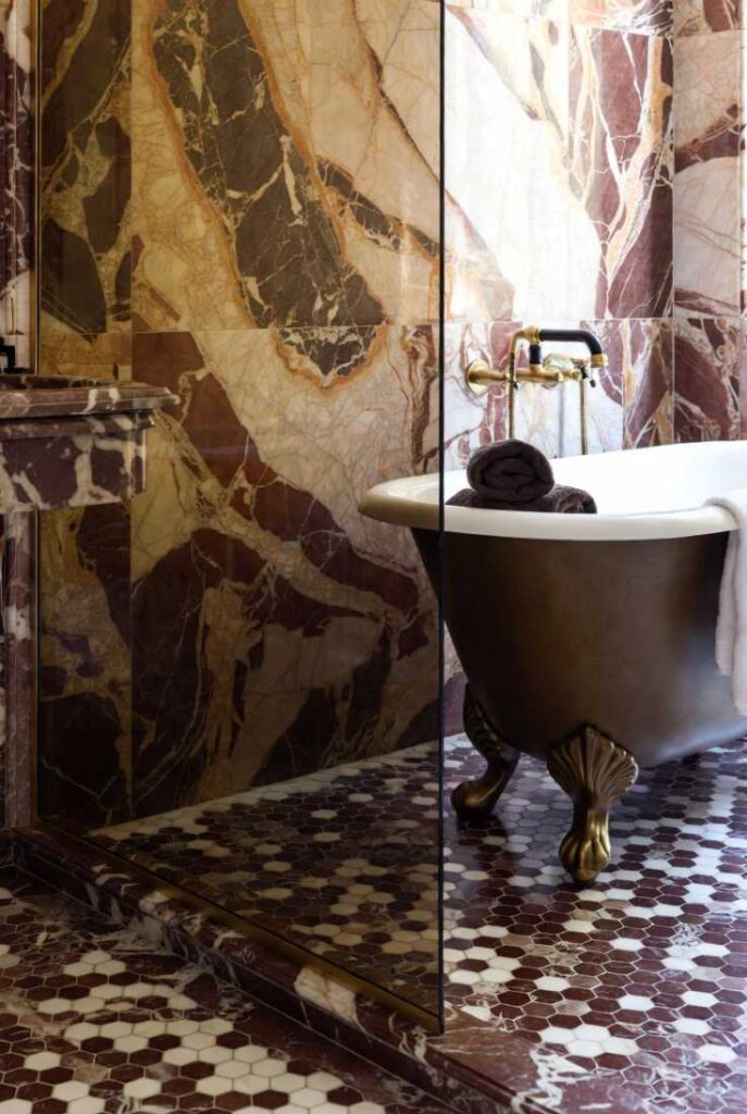 Interior design di un bagno di lusso con pareti e pavimenti in marmo rosso a grandi venature, vasca freestanding scultorea coordinata, piante verdi e illuminazione d'atmosfera.