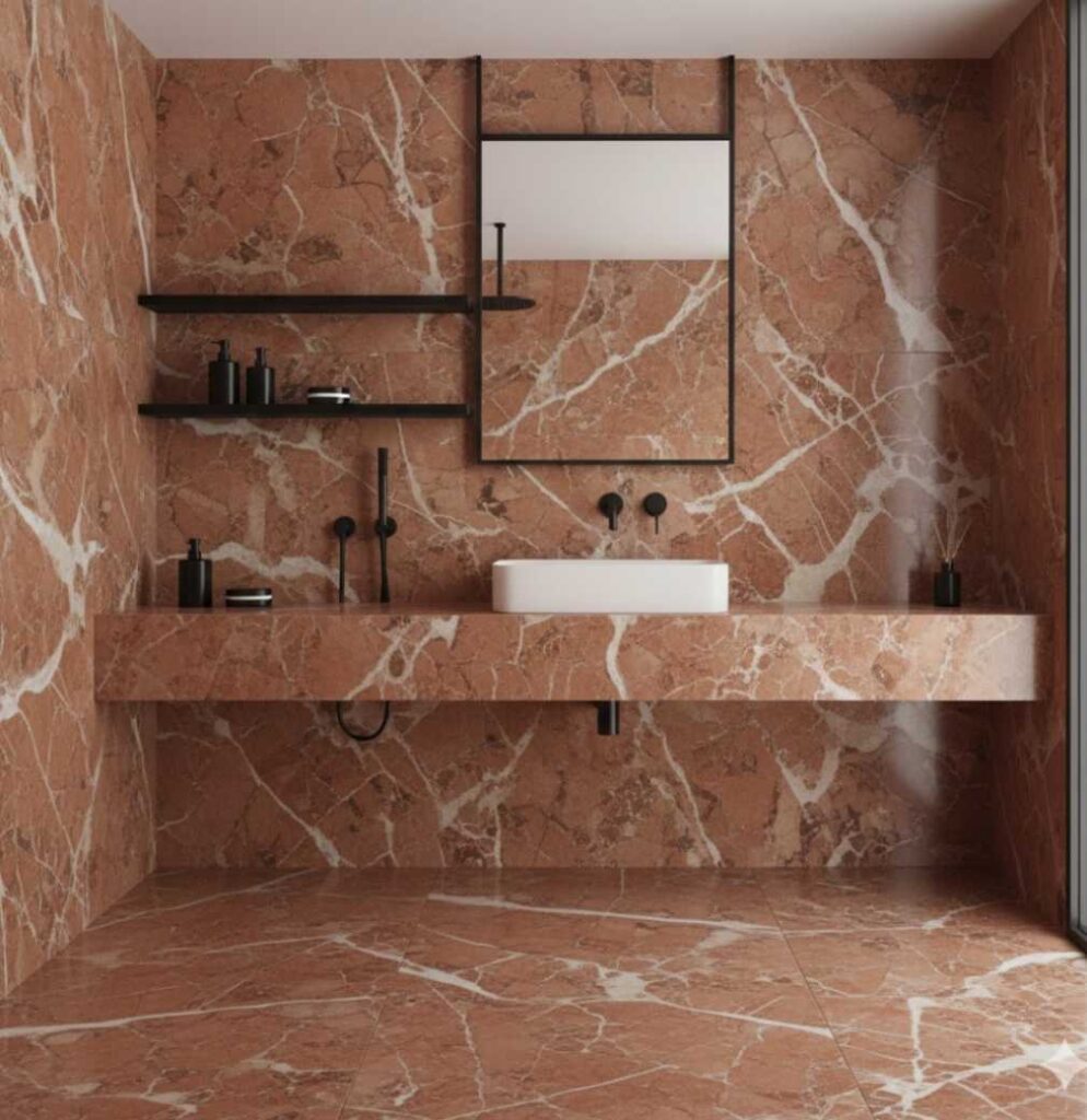 Arredo bagno moderno con pareti in marmo rosso Verona, rubinetteria nero opaco minimale, lavabo bianco d'appoggio su top in marmo e mensole nere sospese.