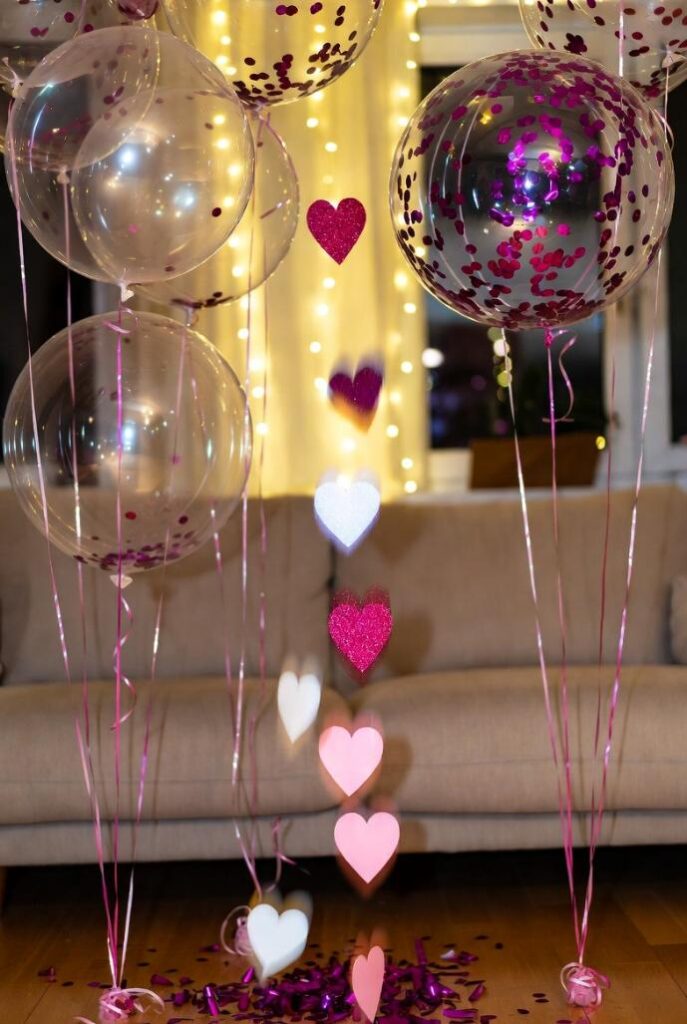 Decorare casa per San Valentino con palloncini confetto: trasparenti riempiti coriandoli rosa glitter, cuori sospesi, luci LED su divano