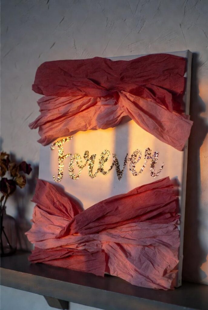 Decorare casa per San Valentino con quadro effimero DIY: carta crespa rosa incollata tela, parola "Forever" glitter oro scintillante su mensola