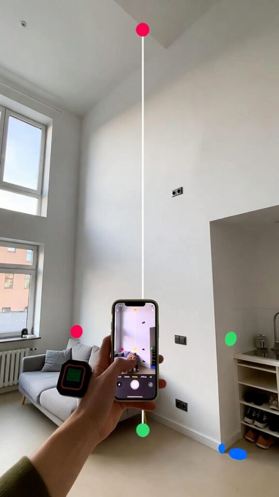 Giovane adulto misura pareti alte in soggiorno moderno con metro laser e app AR su smartphone, adesivi colorati evidenziano zone per arredamento verticale, atmosfera luminosa e pratica 2026.