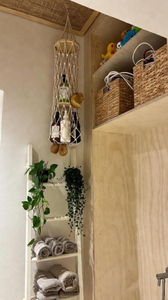 Design d'interni bagno moderno pratico con scala in legno per asciugamani, organizer rete macramè per saponi e spugne, ceste vimini naturali, piante pendenti verdi e luce morbida ad alta risoluzione