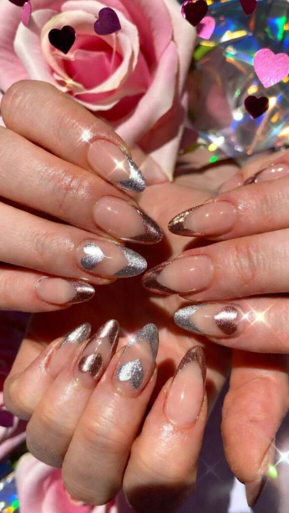 Unghie per San Valentino 2026 nude almond con french glitter argento oro rosa, cuori rosa holo e petali sfondo romantico