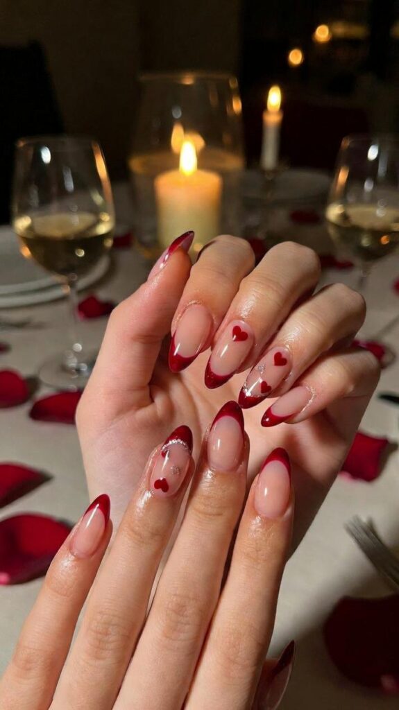 Unghie per San Valentino 2026 French manicure rivisitato con punte rosse curve, cuori bianchi su nude, cena candele vino petali sfondo