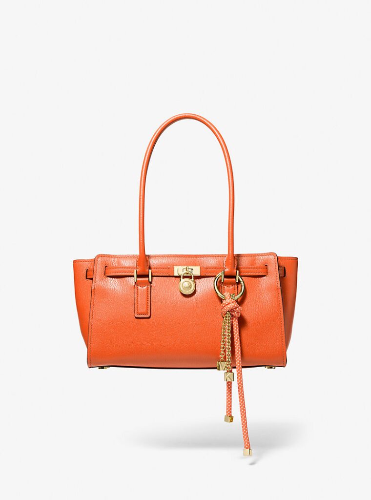 MICHAEL Michael Kors Borsa a mano Hamilton Moderne piccola in pelle arancione con dettagli dorati, lucchetto con logo e foulard decorativo a pois, fotografata su uno sfondo bianco pulito.