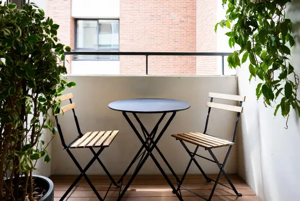 Balcone piccolo con tavolino rotondo pieghevole e due sedie in legno tra piante verdi