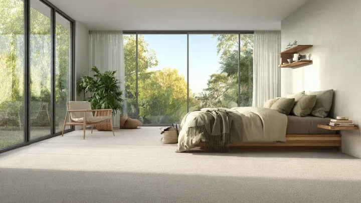 Moquette a pavimento intero in camera da letto moderna luminosa - beige naturale Camera da letto moderna e luminosa con moquette beige chiaro a tutta superficie, letto basso in legno e grandi vetrate sul verde