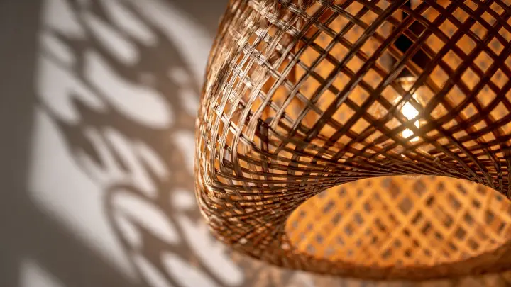 Primo piano di paralume in rattan intrecciato con luce accesa che proietta ombre decorative sulla parete