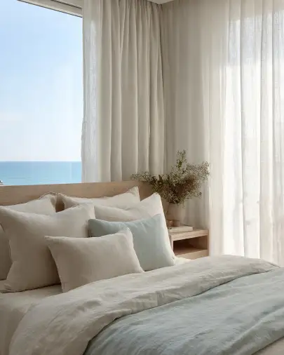 Camera da letto casa al mare con biancheria in lino e vista sull'oceano Camera da letto in stile mediterraneo con biancheria in lino bianco e celeste, tende leggere e vista sul mare