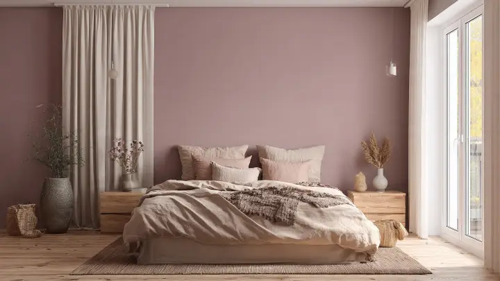 Camera letto parete malva biancheria beige cuscini rosa Camera da letto con parete color malva antico, letto basso con biancheria beige e cuscini rosa cipria, comodini in legno naturale