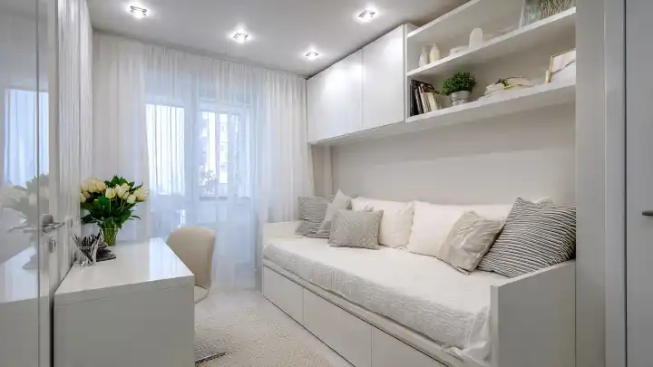 Letto con cassetti contenitori e libreria sospesa per ottimizzare lo spazio in una stanza piccola Letto singolo con cassettoni contenitori integrati e libreria pensile bianca in una camera piccola dallo stile minimal