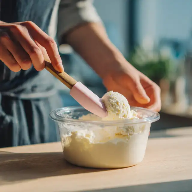 Persona che mescola gelato fatto in casa cremoso in un contenitore con spatola in silicone