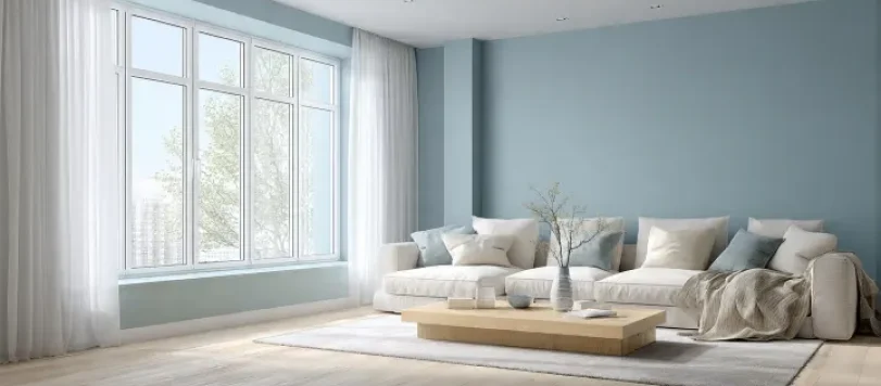 Soggiorno luminoso con pareti celeste polvere, divano bianco e tavolino in legno chiaro su parquet