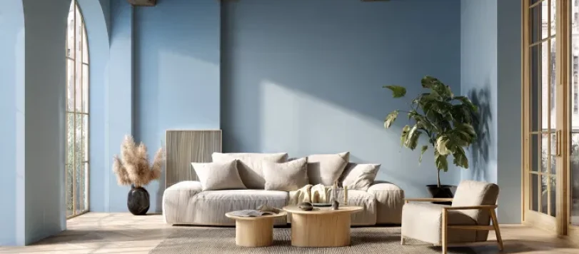 Salotto moderno con pareti celeste polvere, divano beige chiaro, tavolini in legno naturale, pavimento a spina di pesce chiaro, travi in legno a soffitto e finestre ad arco. Atmosfera luminosa, elegante e stile scandi-italiano.