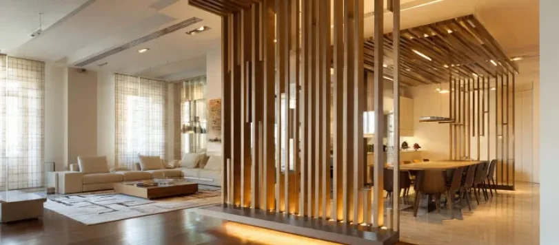Interno di appartamento open space di design italiano, senza pareti divisorie. Soggiorno e cucina separati da parete in doghe verticali di legno e vetro. Colori neutri caldi, arredi eleganti, luce naturale e fotografia architettonica realistica. Composizione pulita, formato 16:9, senza persone.