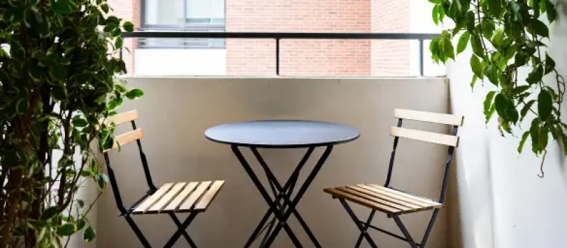 Balcone piccolo con tavolino rotondo pieghevole e due sedie in legno tra piante verdi